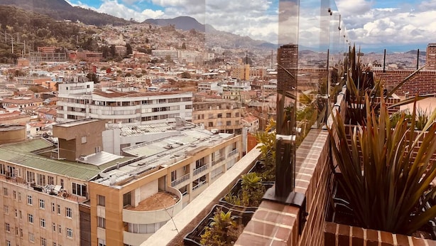 A high-rise building with a rooftop garden and a view of a cityscape with mountains in the background.