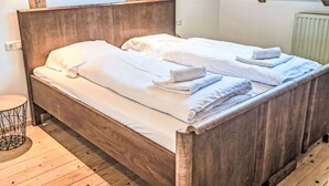 Una cama de madera con sábanas y toallas blancas, una mesita redonda y un tragaluz.