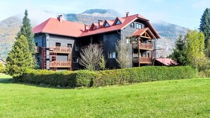 Una cabaña de dos pisos con techo rojo, balcones de madera y montañas al fondo.