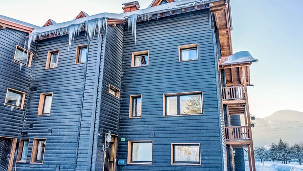 Un edificio de madera de varios pisos, con varias ventanas y un balcón, rodeado de nieve.