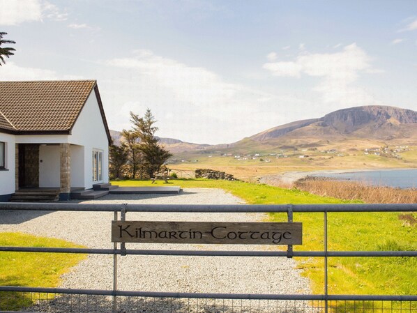 Una cabaña llamada 'Kilmartin Cottage' con un camino de grava que conduce a un edificio blanco con techo de tejas.