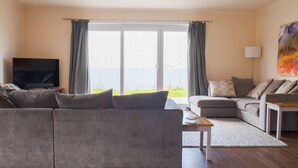 Ein Wohnzimmer mit grauem Sofa, einem kleineren Sofa, einem Couchtisch und einem Fernseher auf einem Schrank.