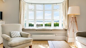 A room with a bay window, a chair with a patterned cushion, a floor lamp, and a sofa.