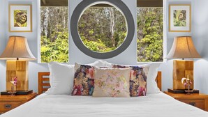A bedroom with a large bed, two bedside tables with lamps, floral-patterned pillows, and framed pictures on the walls. - NEW! Volcano Tea House Cottage 2-HotTub-FirePlace (Volcano)