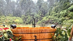 A wooden bathtub with two wine glasses, a bowl of fruit, and candles in a garden setting. - NEW! Volcano Tea House Cottage 2-HotTub-FirePlace (Volcano)