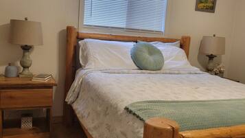 A bedroom with a wooden bed, two bedside tables with lamps, a window with blinds, and a patterned rug.