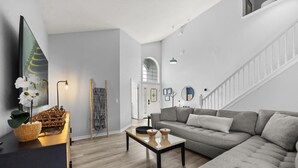 Uma sala de estar moderna com um sofá cinzento, uma mesa de centro de madeira e uma cesta de vime com flores.