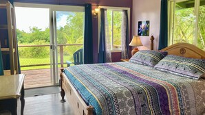 A bedroom with a large bed, a wooden nightstand, a chair, and a view of a garden through a sliding glass door.