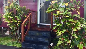 A house with a wooden staircase leading to a glass door, surrounded by lush greenery.