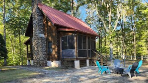 A stone cabin with a red roof, large windows, and a porch with outdoor seating.