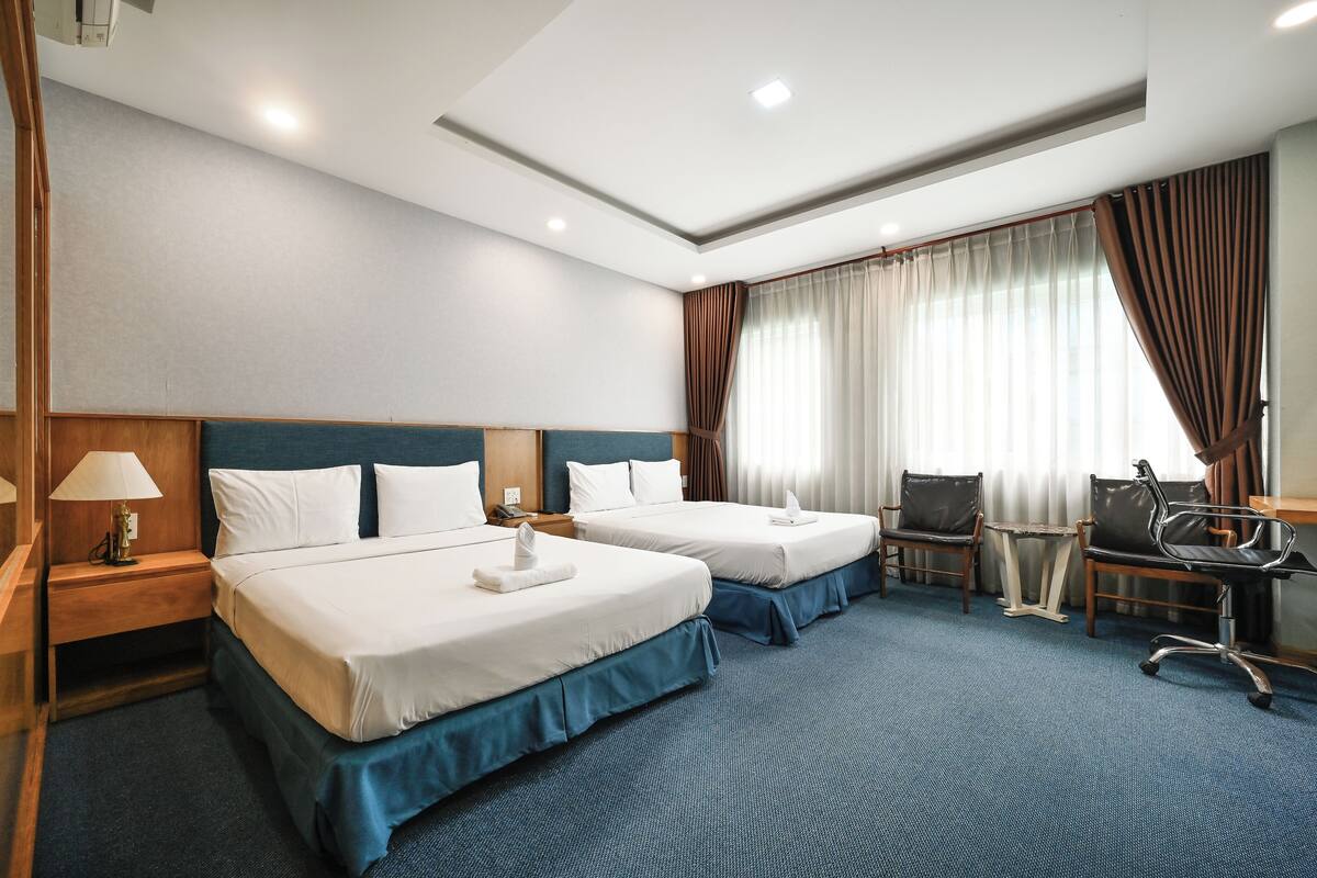 Habitación de hotel con dos camas, un escritorio, una silla y una lámpara.
