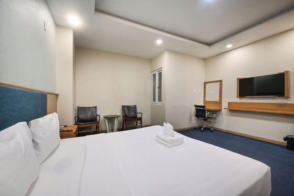 A hotel room with a large bed, two chairs, a desk, a television, and a window.