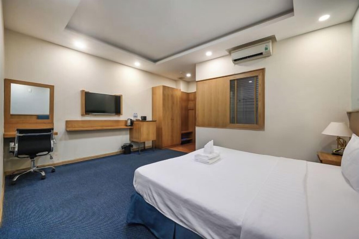 A hotel room with a bed, a desk, a chair, a television, and a wardrobe.