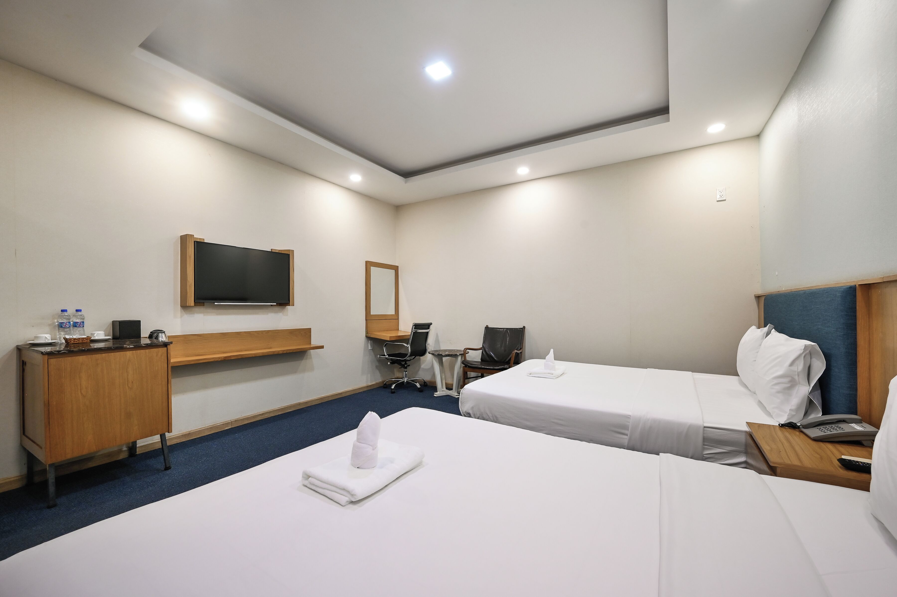 Une chambre d’hôtel avec deux lits, un bureau, une chaise, une télévision et une petite table.