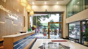 A reception area with a wooden reception desk, a neon sign for Sunshine Airport Hotel, and a view of the outside through large glass doors. - Sunshine Airport Hotel (Ho Chi Minh City)