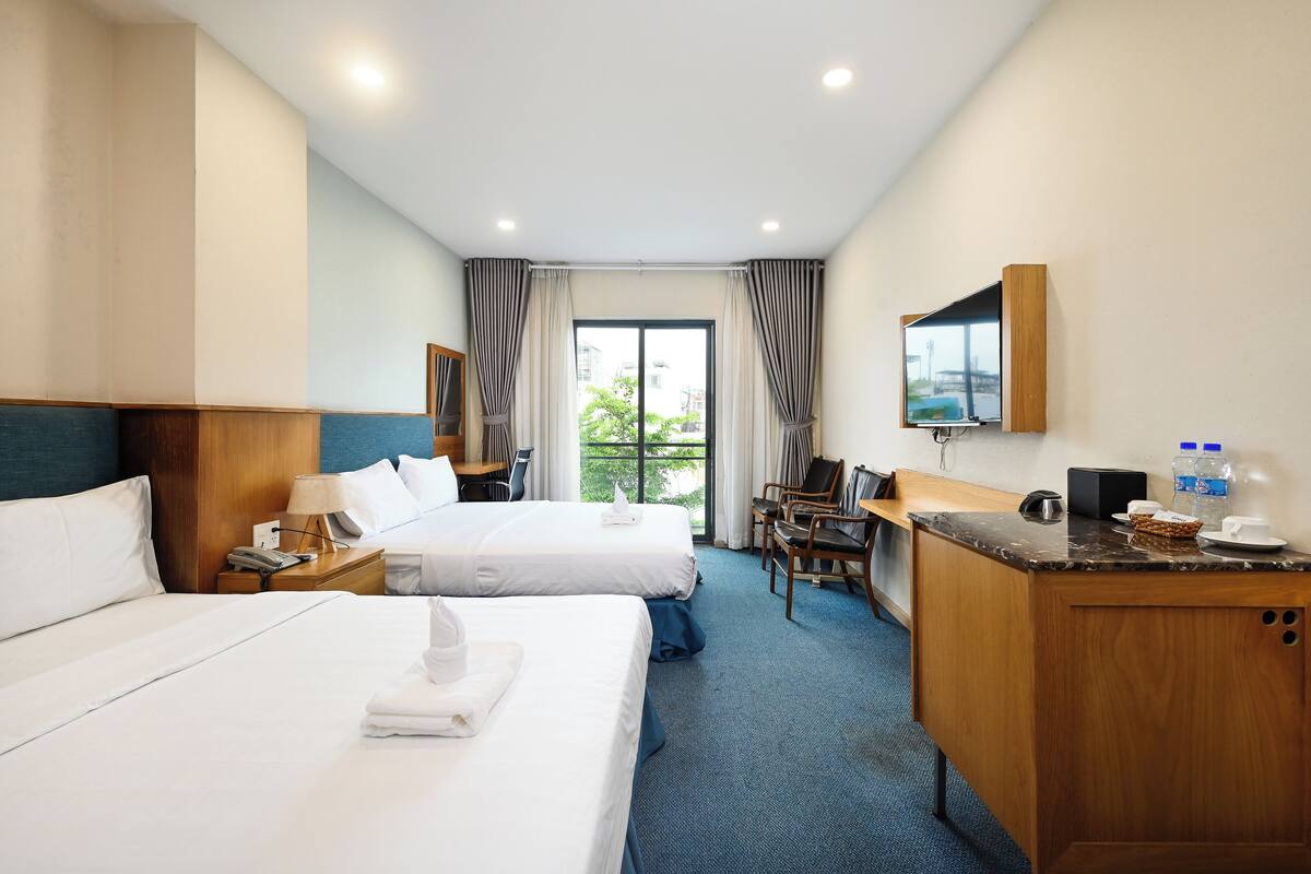 Habitación de hotel con dos camas, un escritorio, una silla, un televisor y una ventana con cortinas.