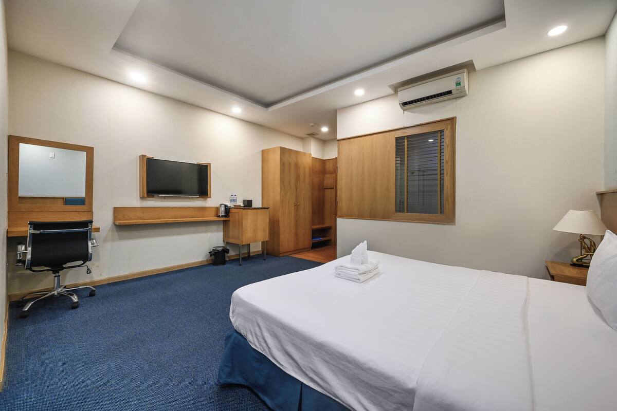 Una habitación de hotel con cama, escritorio, silla, armario y televisor.