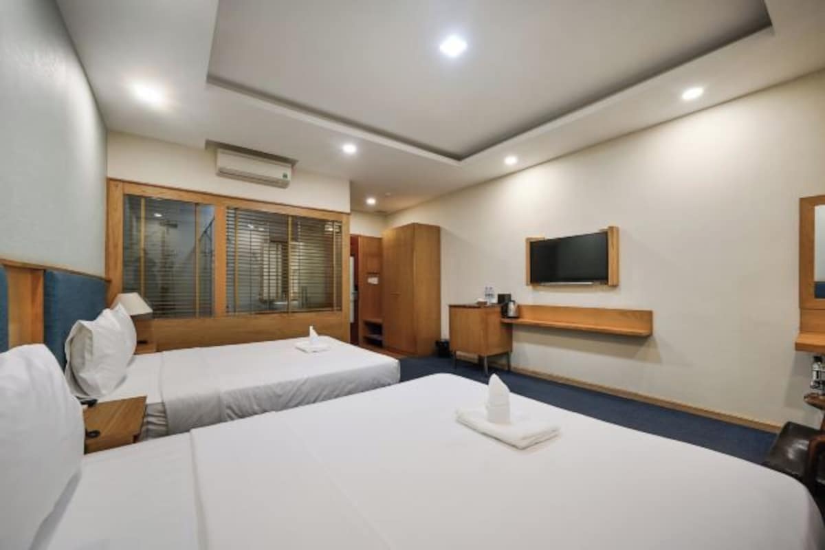 Habitación de hotel con dos camas, un escritorio, un televisor y una ventana con persianas.