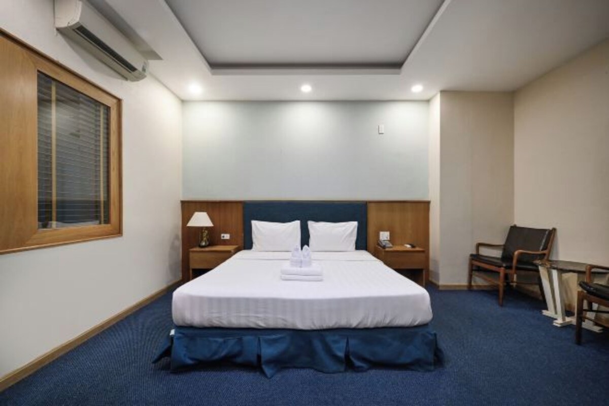 Una habitación de hotel con una cama grande, un escritorio, una silla y una ventana con persianas.