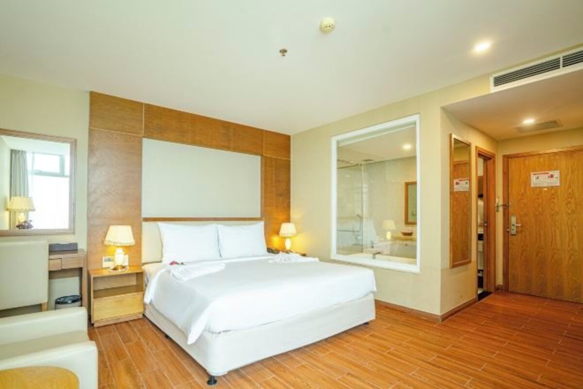 Habitación de hotel con una cama grande, lámparas de noche, cabecero de madera, un espejo grande y una puerta de madera.