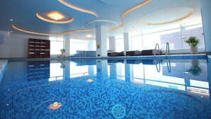 Una piscina interior con suelo de mosaico azul, iluminación empotrada y una zona de estar con una planta.