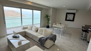 Uma sala de estar moderna com uma grande janela com vista para uma paisagem deslumbrante, uma área de estar com sofá e mesa de centro, e um espaço de jantar com mesa e cadeiras.