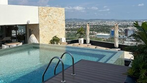 Uma piscina infinita com um deque de madeira, uma parede de pedra e vista para um horizonte urbano.