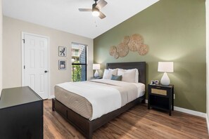 A bedroom with a bed, two bedside tables with lamps, a ceiling fan, and a door.