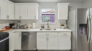 A modern kitchen with white cabinets, stainless steel appliances, and a window with a view of a purple building.