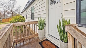 A wooden deck with a welcome mat, a white door, and two potted plants.