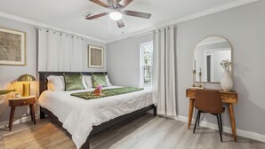 A bedroom with a bed, a desk, a chair, a ceiling fan, and a window.