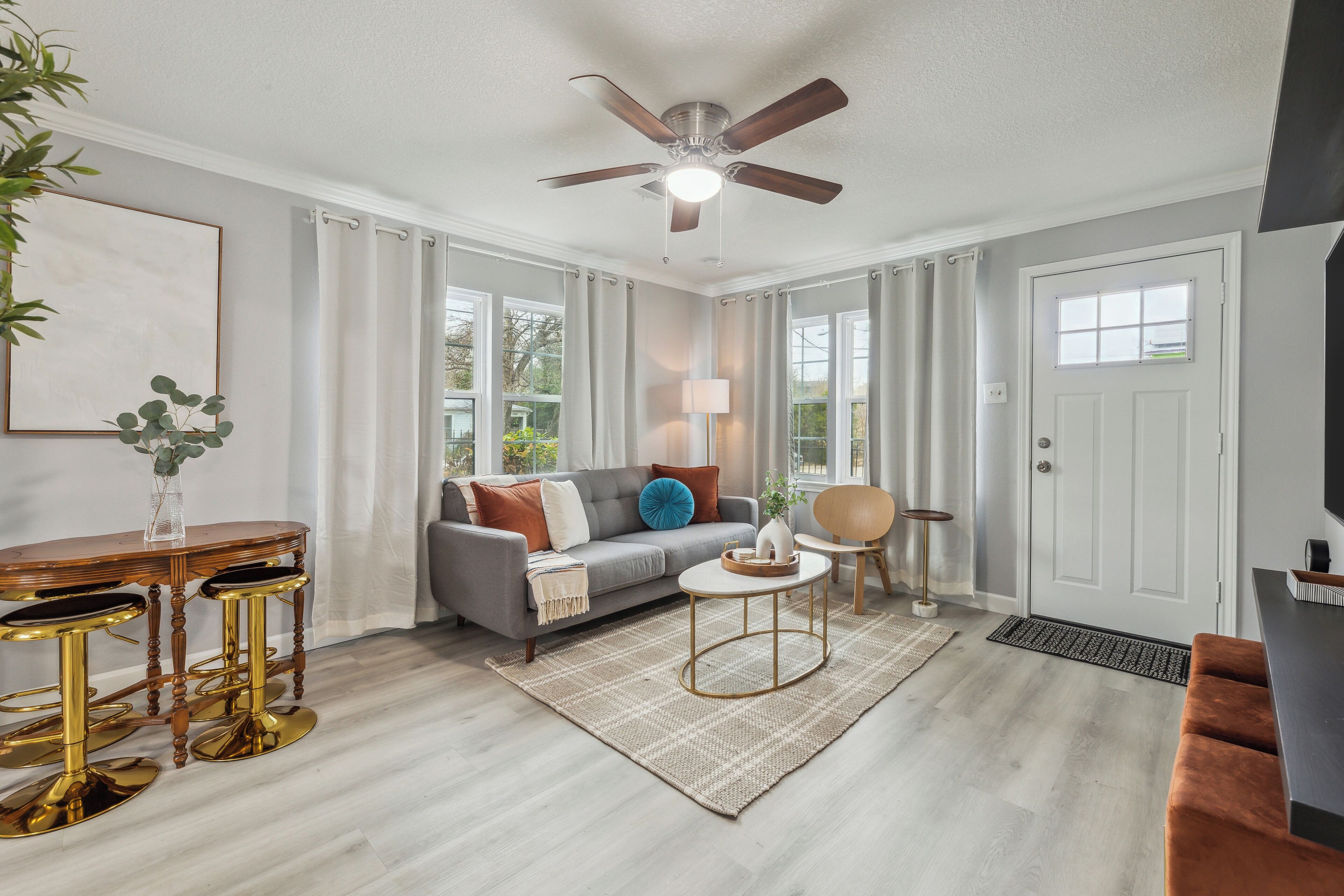 Un salon moderne avec un canapé gris, un ventilateur de plafond, une table basse et un tabouret de bar.