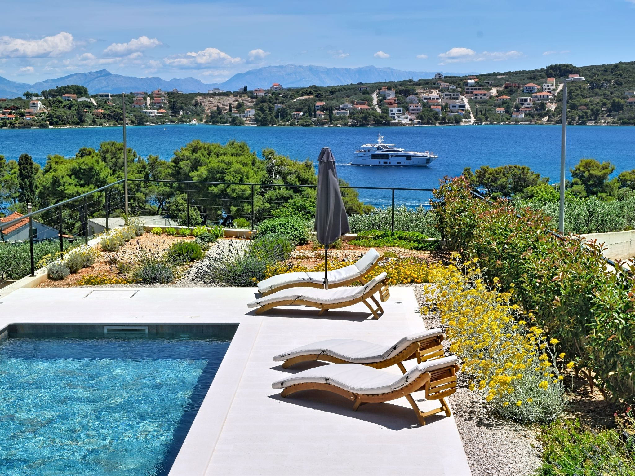 A pool area with lounge chairs and a view of a body of water with a yacht.