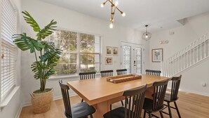 A dining area with a wooden table, black chairs, a large potted plant, and a chandelier. - Modern Villa w/ Pool, Hot Tub & Theater Room! (Kissimmee)