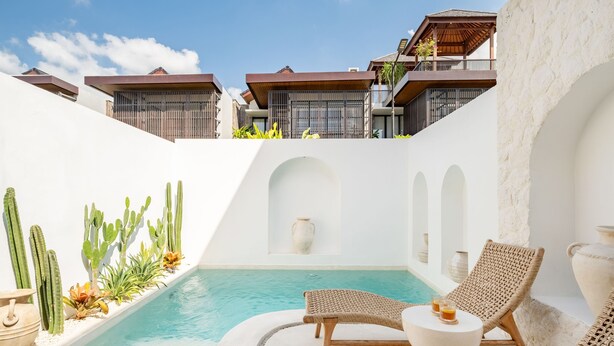 A pool area with lounge chairs and cacti, surrounded by white walls and a clear blue sky. - Casa Blanche Canggu (Canggu)