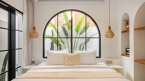 A bedroom with a large window, a bed with white bedding, two bedside tables, and a hanging light fixture. - Casa Blanche Canggu (Canggu)