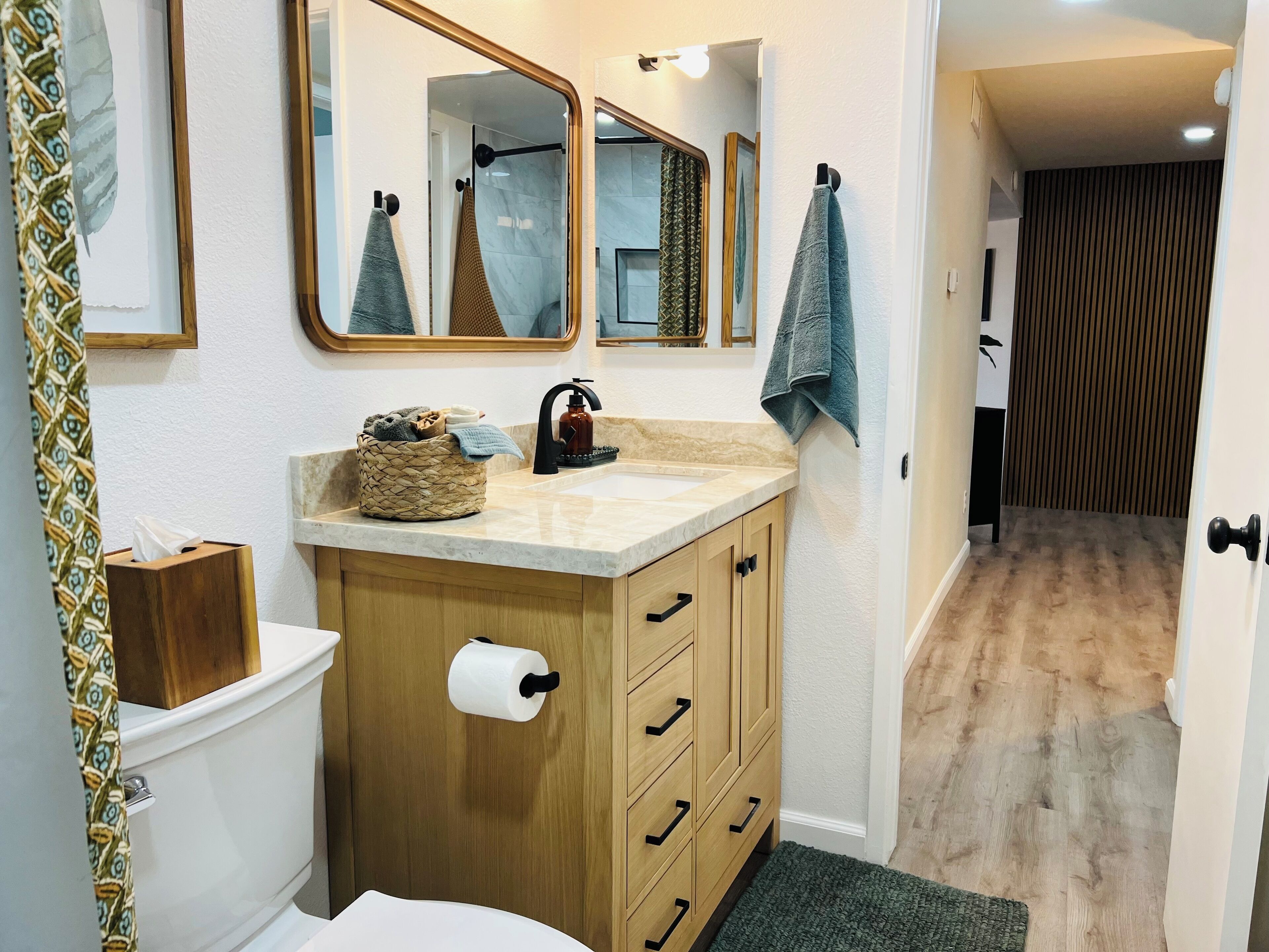 Une salle de bain avec un meuble-lavabo en bois, des toilettes, un lavabo avec un distributeur de savon et une serviette accrochée au mur.