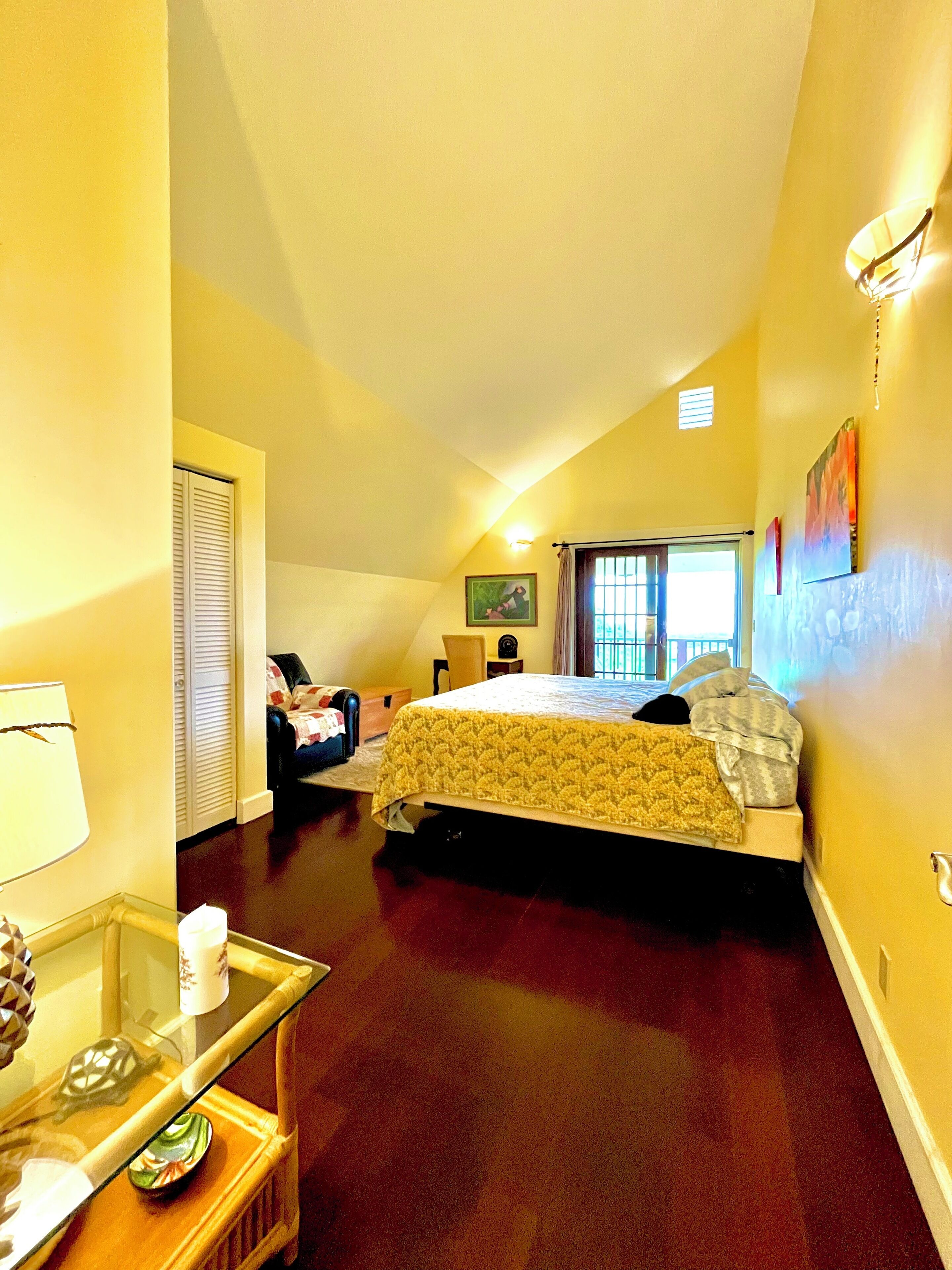 A bedroom with a bed, a chair, a table with a lamp, and a window with curtains.