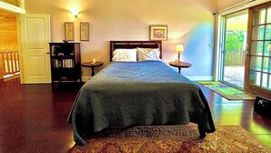 Une chambre à coucher avec un grand lit, une table de chevet avec une lampe, une bibliothèque et une porte donnant sur un balcon.