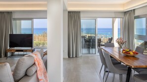 Een moderne hotelkamer met een ruim balkon, een zithoek met een schaal fruit, en een flatscreen televisie.