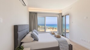 Een moderne slaapkamer met een groot bed, uitzicht op het strand en een schuifdeur.