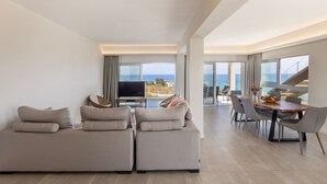Een moderne woonkamer met een grote zithoek, een flatscreen televisie en een eetgedeelte met uitzicht op zee.
