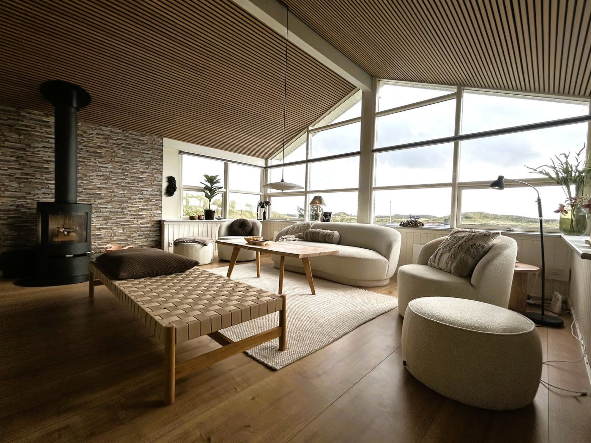 A modern living room with a stone wall, a wood-burning stove, a large window, and a view of the outdoors.