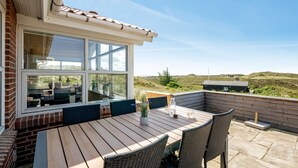 An outdoor patio with a wooden table and wicker chairs, overlooking a grassy landscape.