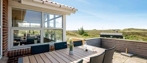 An outdoor patio with a wooden table and wicker chairs, overlooking a grassy landscape.
