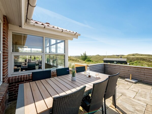 Une terrasse extérieure avec une table en bois et des chaises en osier, donnant sur un paysage verdoyant.