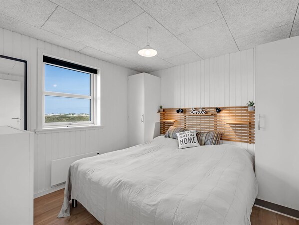 Een slaapkamer met een groot bed, een raam met uitzicht, een hoofdeinde met een bord en een radiator.