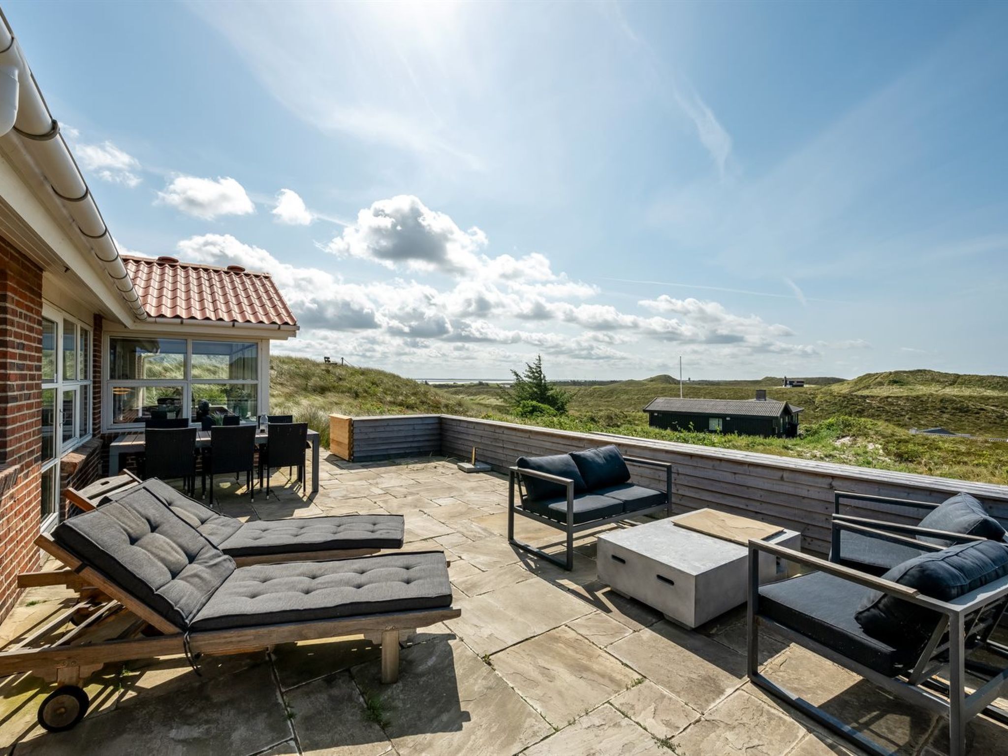 A rooftop patio with lounge chairs, a dining area, and a view of the landscape.
