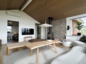 A modern living room with a wooden ceiling, a stone wall, a fireplace, a television, and a sofa.