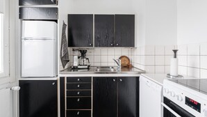 Una cocina moderna con gabinetes negros, un refrigerador blanco, una cafetera y un reloj digital que marca las 14:32.